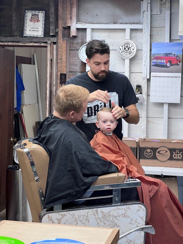 boy getting haircut in small town barbership with dad holding him