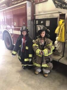 two kids at a fire station dressed in firemans clothing