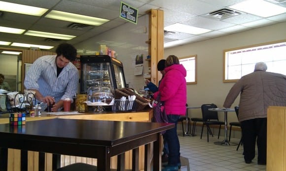 small coffee shop with one man serving and two people adding sugar and cream to their coffee